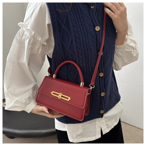 Detail of red crossbody bag with a distinctive golden H-shaped clasp on matte finish