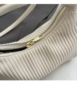 Gros plan sur la fermeture éclair dorée et la texture plissée du sac beige moderne