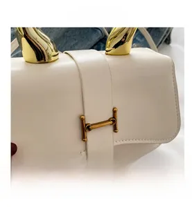 Detailansicht der cremefarbenen Ledertasche mit goldener H-Schnalle und Metallverzierung