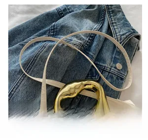 Details einer weißen Ledertasche mit goldenem Metallgriff und verstellbarem Schultergurt