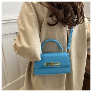 Detail of a bright blue leather handbag featuring a golden clasp on a beige trench coat