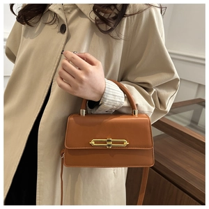 Close-up of a brown leather bag with a unique gold oval lock on a khaki trench coat