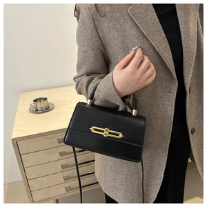 Detail of black leather crossbody bag with gold chain buckle worn over a grey blazer