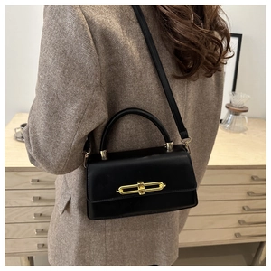 Detailed view of black leather shoulder bag with elegant gold metal buckle on female model