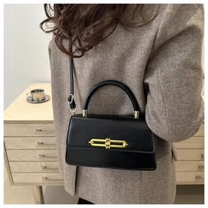 Detail of a black leather shoulder bag with gold chain buckle on a blazer-clad model