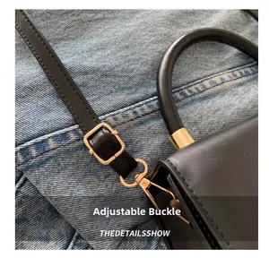 Detailed close-up of the adjustable golden buckle on a black leather handbag strap