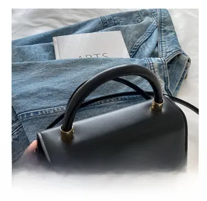 Detail of black leather handbag featuring a bold gold chain buckle and round top handle