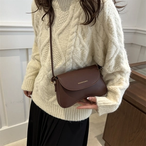 Chic brown saddle crossbody bag for women with gold lettering on a stylish female model