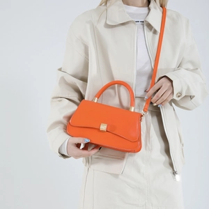Orange leather handbag with gold buckle shown by model for single shoulder and crossbody use