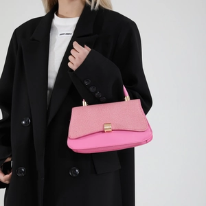 Pink patchwork crossbody bag with textured fabric flap and gold buckle on a black blazer