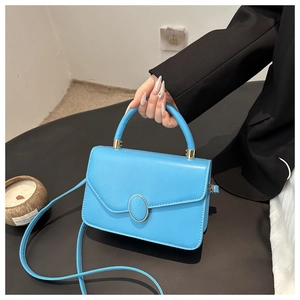 Detail of bright blue faux leather crossbody bag with gold-tone buckle and round handle
