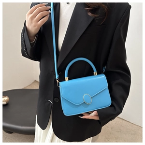 Detail of bright blue leather crossbody bag with oval gold buckle shown on a model