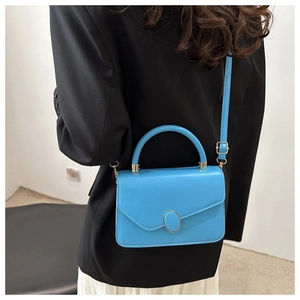 Detail view of bright blue leather crossbody bag with metallic clasp on a dark coat