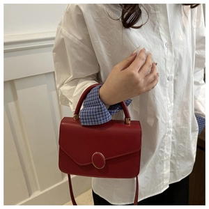Detail of red leather crossbody bag with gold oval buckle and top handle held by a model