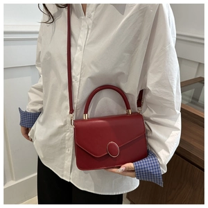 Minimalist red leather handbag with gold buckle shown on model in modern office setting