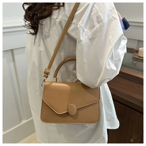 Close-up of caramel leather crossbody bag with gold buckle on an elegant model