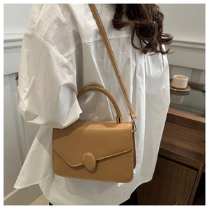 Detail of light brown retro small square bag with metal clasp against a white shirt background