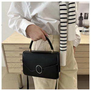 Detail of minimalist black crossbody bag with gold-trimmed oval buckle and smooth texture