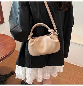Detail of a beige ruched cloud bag worn crossbody over a stylish black leather jacket