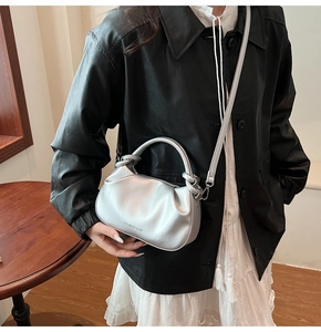 Detail showing metallic silver pleated handbag texture with a round top handle