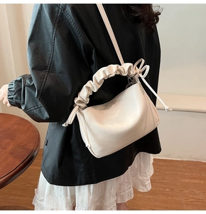 Detail of cream white pleated shoulder bag with knotted handle on a black leather jacket
