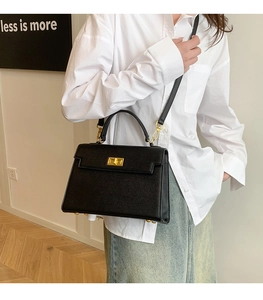 Detailed view of black crossgrain leather handbag with gold metal clasp on a model