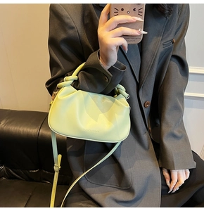 Close-up of a lime yellow pleated handbag with a knotted handle on a grey blazer outfit