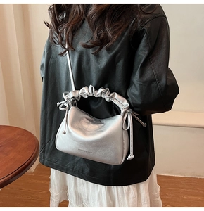 Close-up of silver pleated handbag featuring drawstring details and a thin shoulder strap