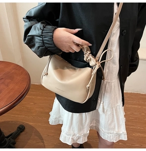 Close-up of beige ruched handbag with drawstring knots and elegant pleated leather handle