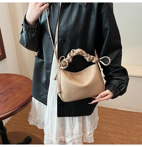 Model wearing a beige pleated hobo bag with bow details and a long shoulder strap