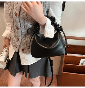 Detail of black pleated hobo bag with ruched handle and side drawstring on model