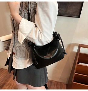 Detail view of black pleated underarm bag with drawstring knot on a model