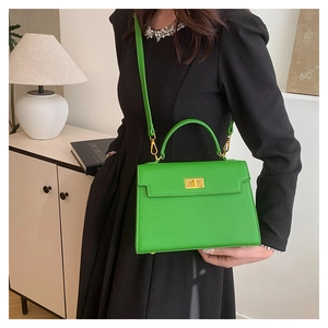 Detail of lime green leather handbag with gold turn-lock and detachable strap on a model