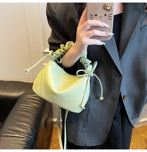 Detail of light green pleated handbag with decorative side bow and logo on premium faux leather