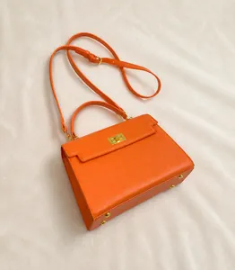 Detail of orange lychee leather handbag featuring a golden turn-lock and metal feet