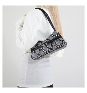 Close-up of snakeskin baguette bag with buckle strap worn under the arm on model