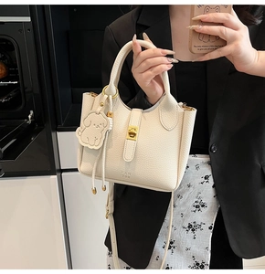 Detail of cream bucket bag with litchi texture, golden turn-lock, and cute dog charm