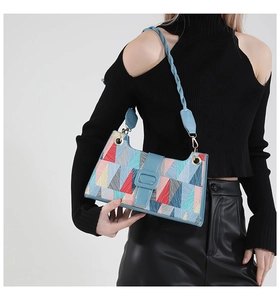 Detail shot of a geometric pattern underarm bag with blue woven strap on black outfit