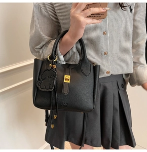 Detail of black lychee leather bucket bag with gold lock and dog pendant on a model