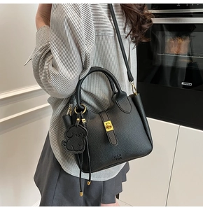 Detail of black lychee grain leather bucket bag with gold twist lock and dog charm