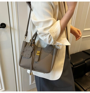 Detail of taupe pebbled leather bucket bag with gold turn-lock and leather puppy charm