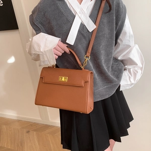 Classic brown leather satchel bag with gold hardware shown on model in modern room