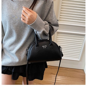 Detail of black pebbled leather shell bag with white text and silver metal hardware strap