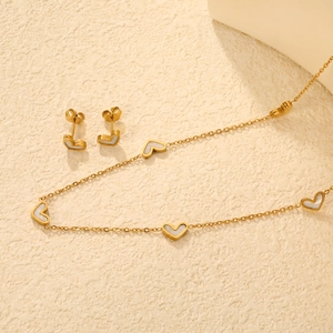 Golden stainless steel jewelry set with white heart shell pendants on stone background