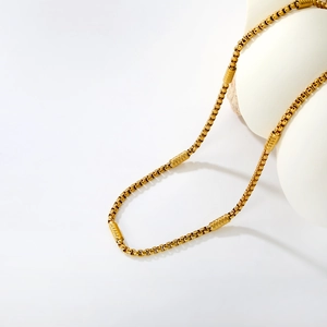 Golden stainless steel box chain necklace with cylindrical beads on a white pedestal