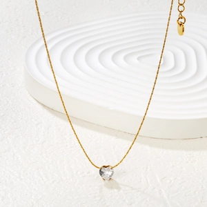Elegant gold heart zircon pendant necklace displayed on a textured white ripple plate