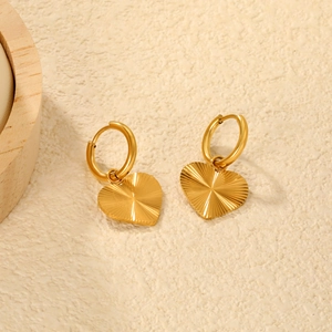 Gros plan de boucles d'oreilles cœur dorées avec textures rayonnantes sur pierre