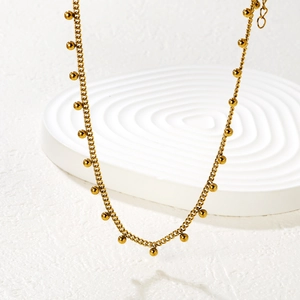 Close-up of golden beaded chain necklace displayed on white textured display stand