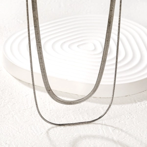 Close-up of silver layered herringbone snake chain and thin link necklace on pedestal