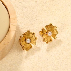 Élégantes boucles d'oreilles fleur en or avec perle sur fond chaud et texturé